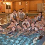 Group of young people sitting on steps into shallow swimming pool some wearing blue medallions